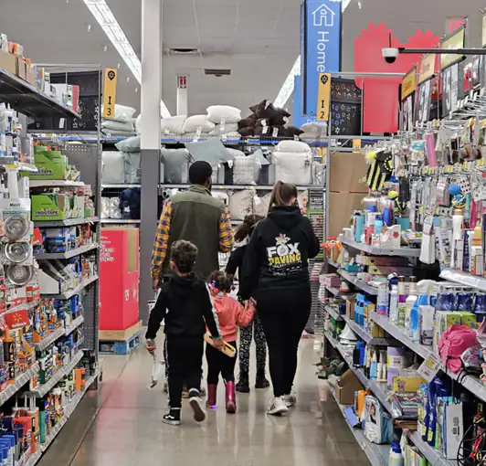 A parent and two children walking down a Walmart aisle lined with household goods